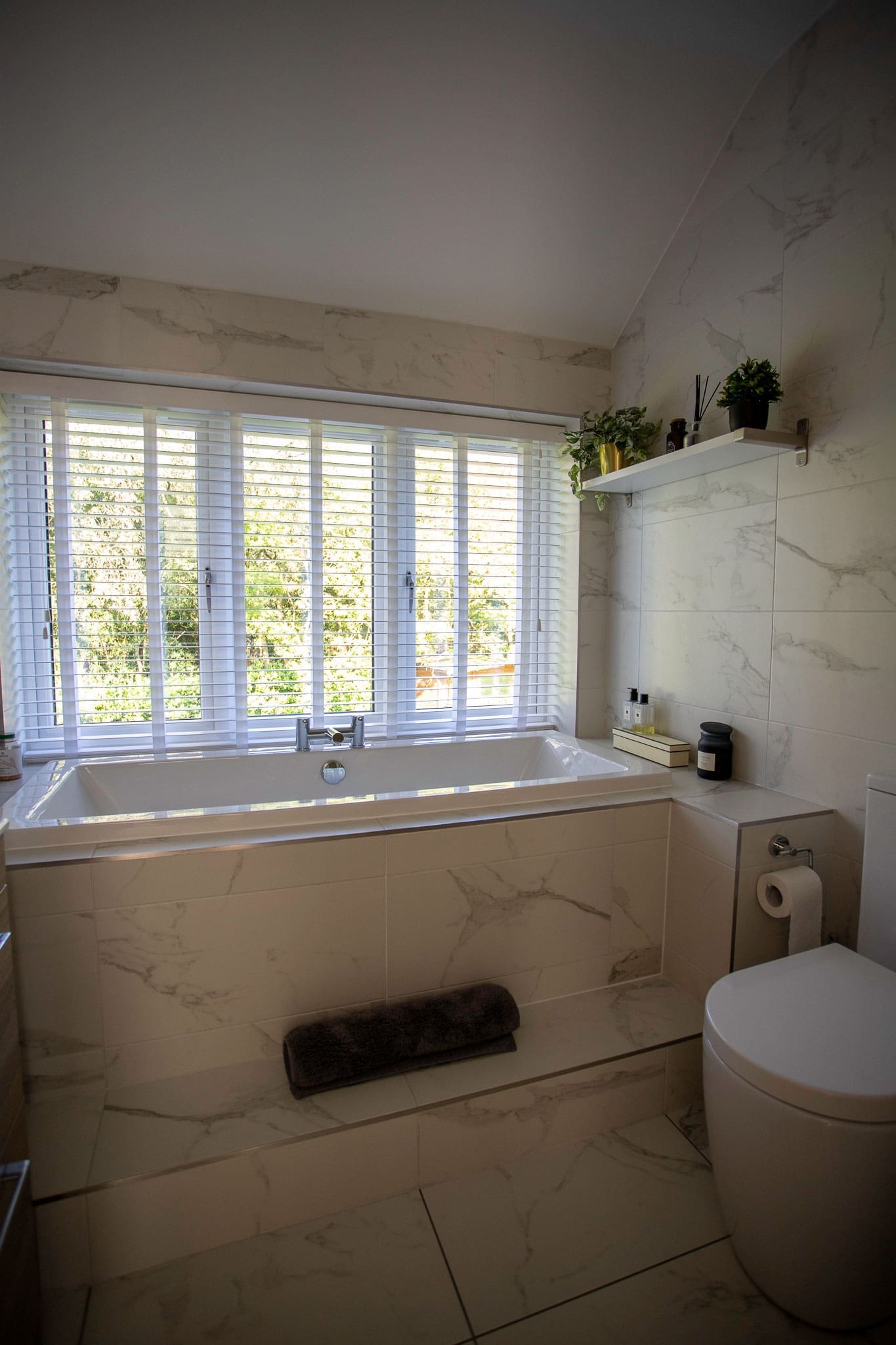 Light bathroom with marble-effect tiles and a fitted bath beneath the window.