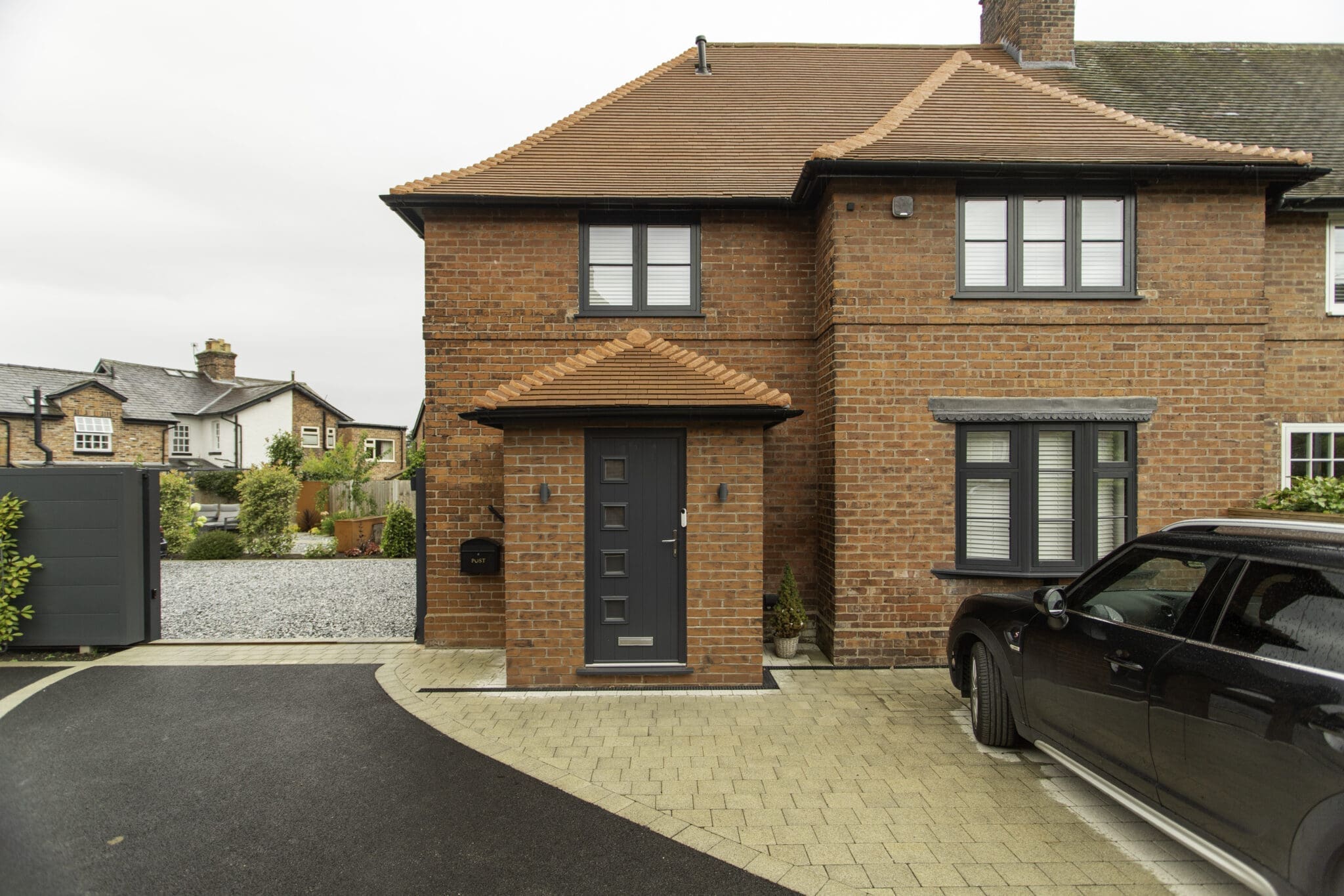 Front elevation of the brick house with a tiled entrance porch, dark-framed windows and paved driveway.