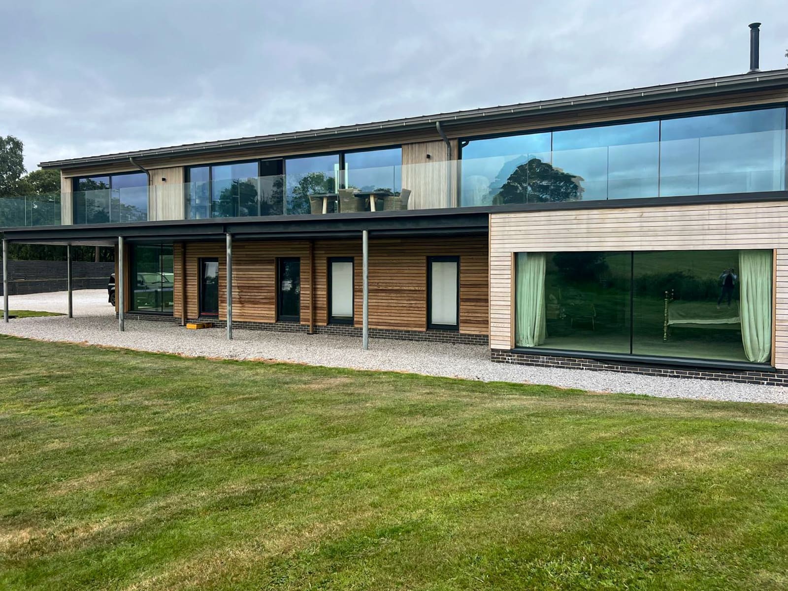 Timber-clad elevation with full-height glazing and a glass-balustraded first-floor terrace.
