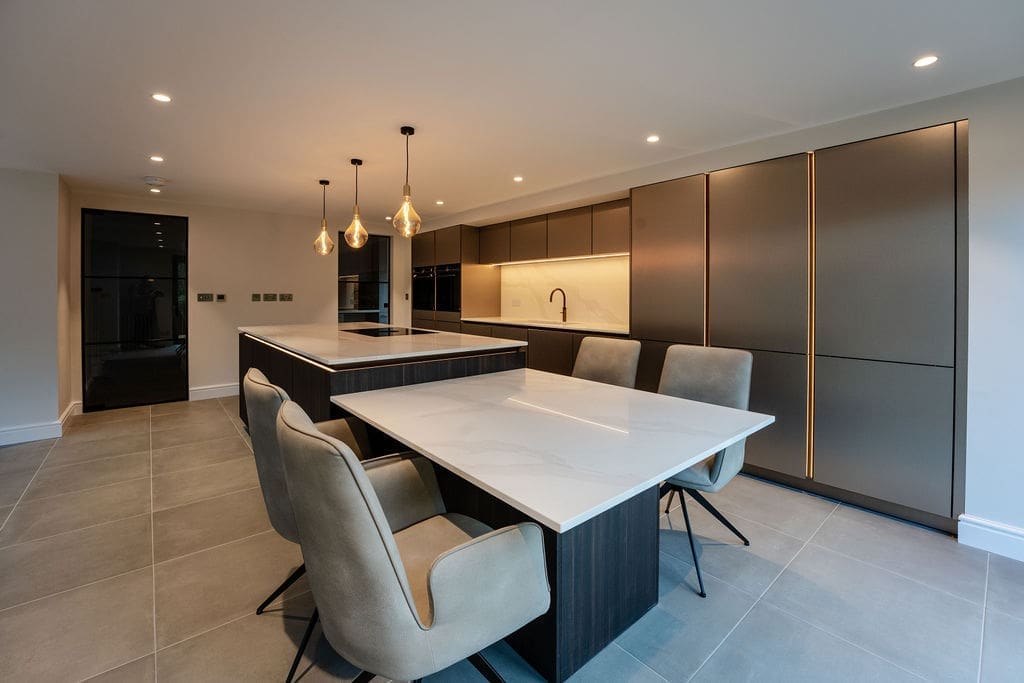 Open-plan kitchen and dining area with a marble-effect table, dark cabinets and pendant lighting.
