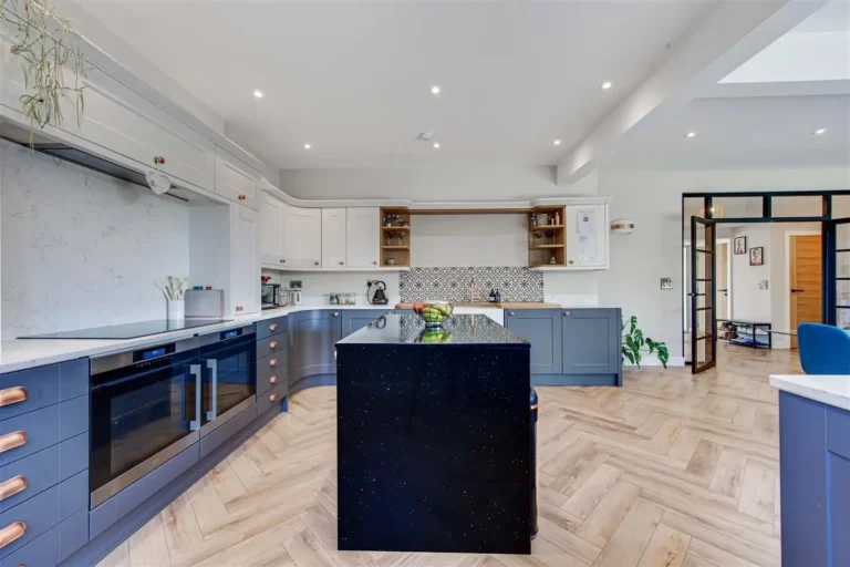 Contemporary kitchen with a dark island, blue cabinetry, copper handles and a patterned splashback